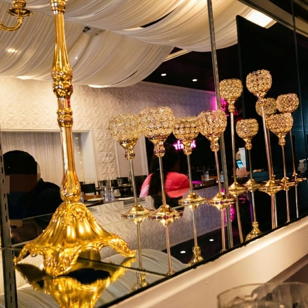 Ornate golden candelabras and crystal candle holders reflecting in a mirrored surface inside a restaurant.
