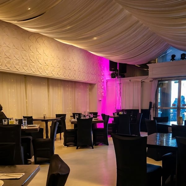 A restaurant dining room with a couple seated at a table, draped ceilings, and pink accent lighting.