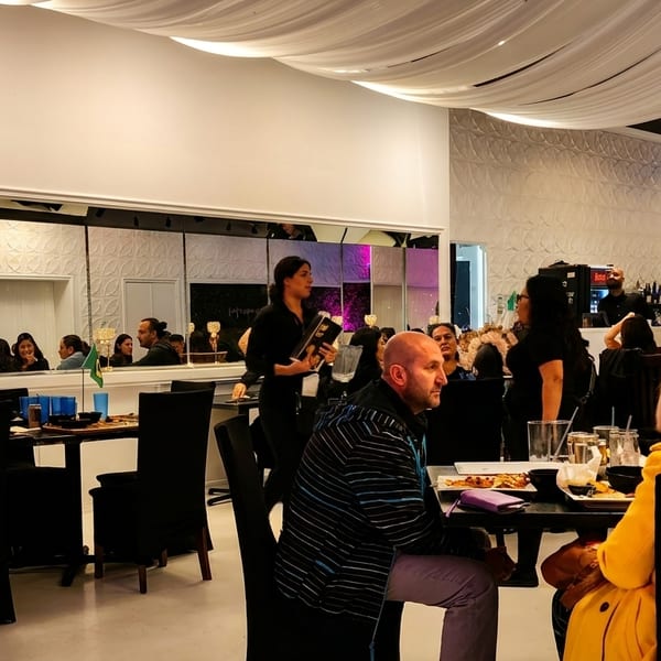 Diners seated at tables in a brightly lit restaurant with white walls and a lush plant wall.
