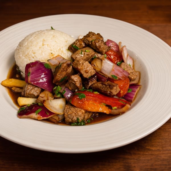 Sautéed beef with tomatoes, onions, and peppers served in brown sauce alongside a mound of white rice.