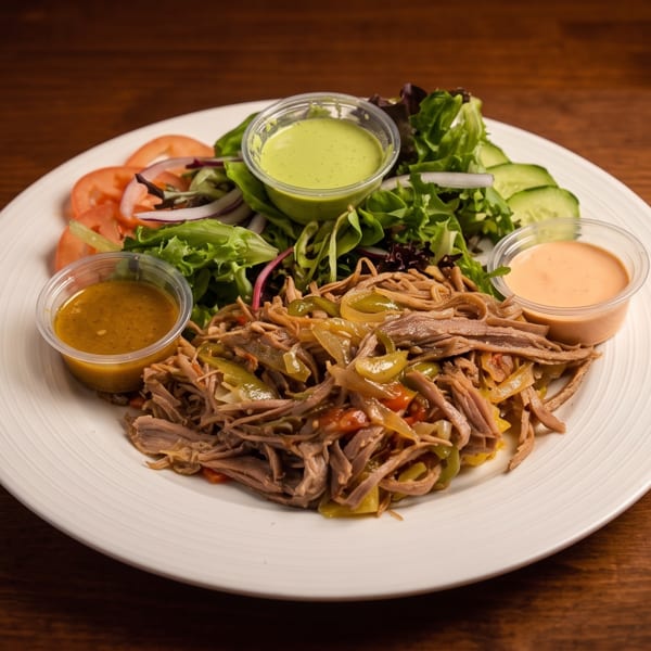 Plate of shredded beef with sautéed peppers, salad, and three dipping sauces on a wooden table.