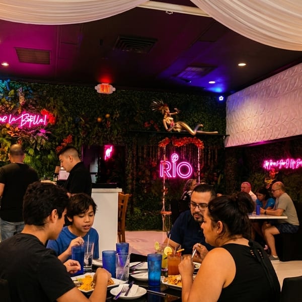 Diners enjoy meals in a vibrant restaurant with neon signs, lush green walls, and white draped ceilings.